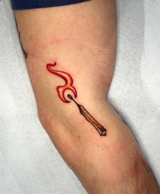 Paintbrush with flowing red and yellow flames on the calf of a leg against a light background.