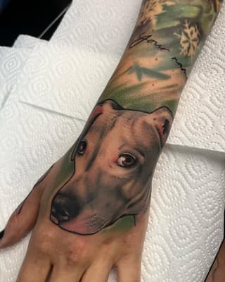 Portrait of a dog's face on the hand and forearm with green and brown coloring, featuring detailed eyes and shading.