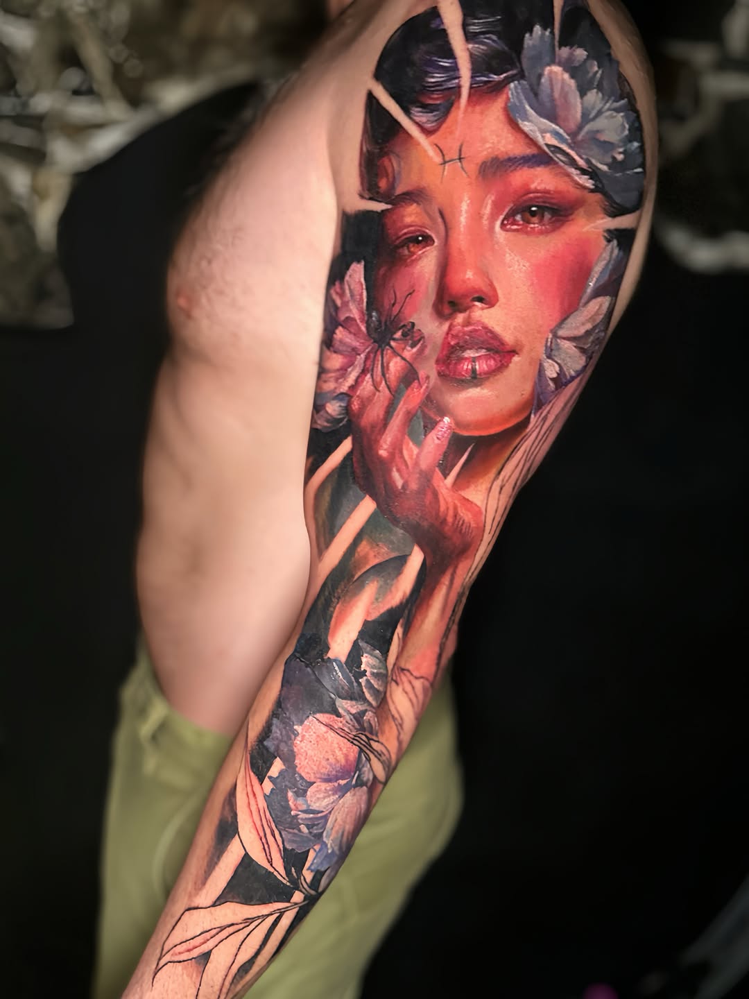 Photorealistic portrait of a woman's face with red tones, surrounded by floral elements, on upper arm sleeve.