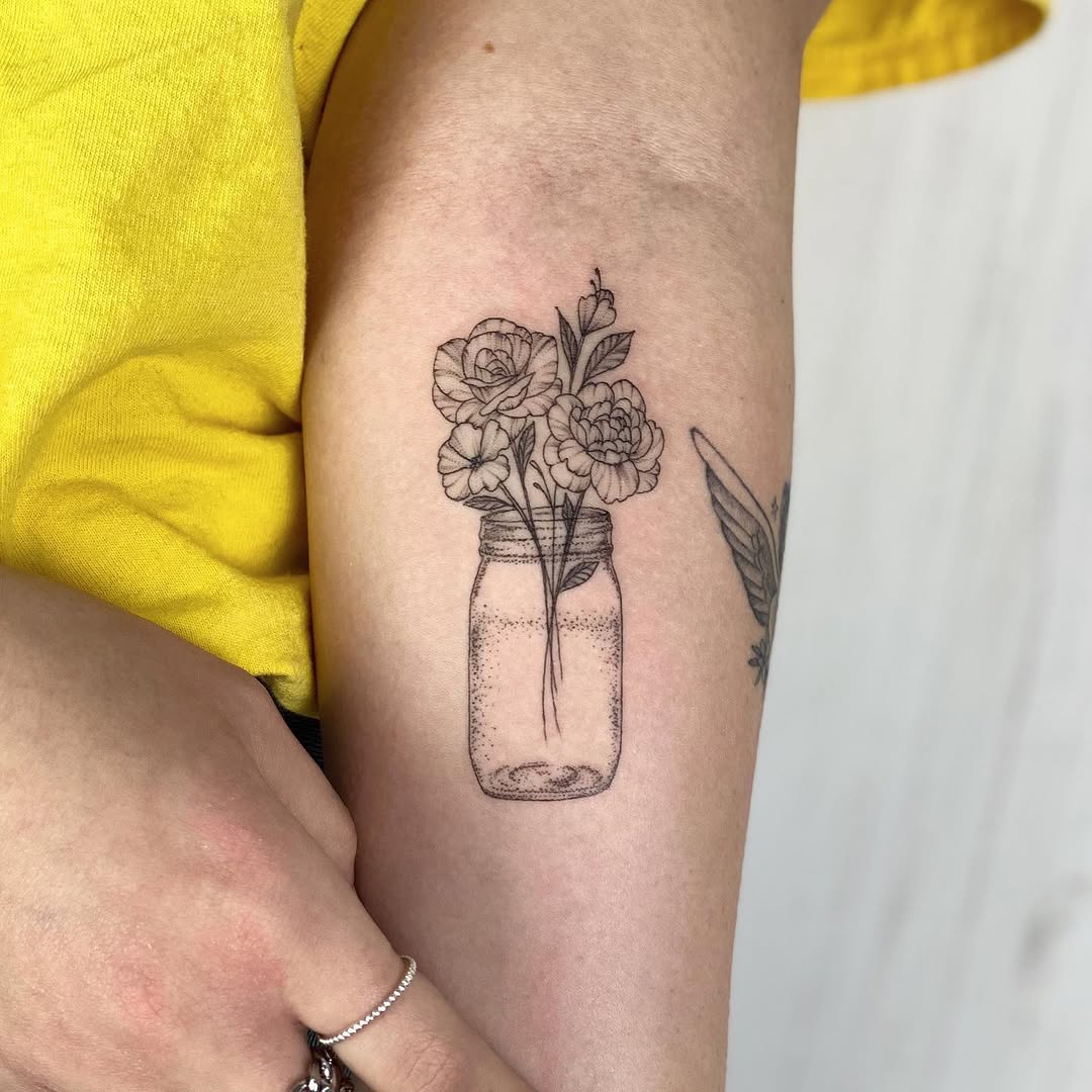 Fine-line tattoo of roses in a glass jar with delicate linework on the upper arm.