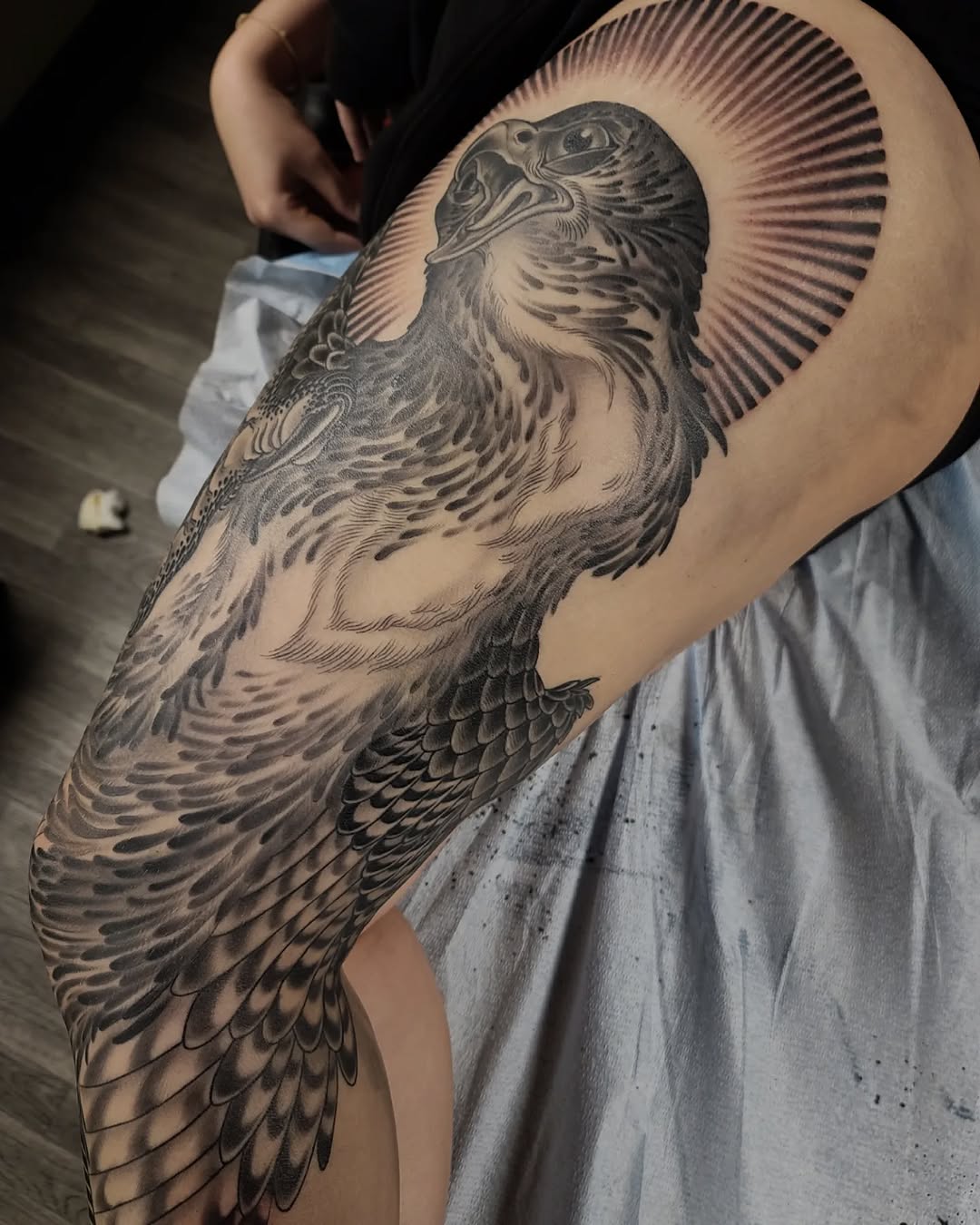 Black and grey eagle tattoo with detailed feathering and radiating halo lines on upper arm.