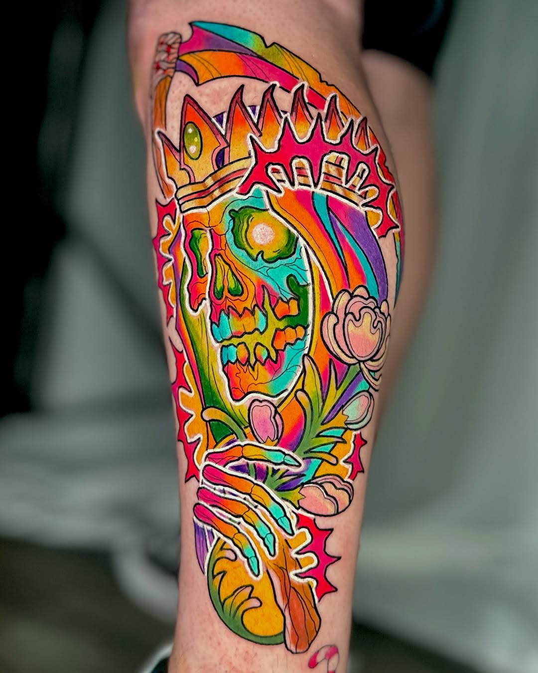 A colorful skull with rainbow striping, floral elements, and decorative spikes on the calf, executed in vibrant multi-color ink.