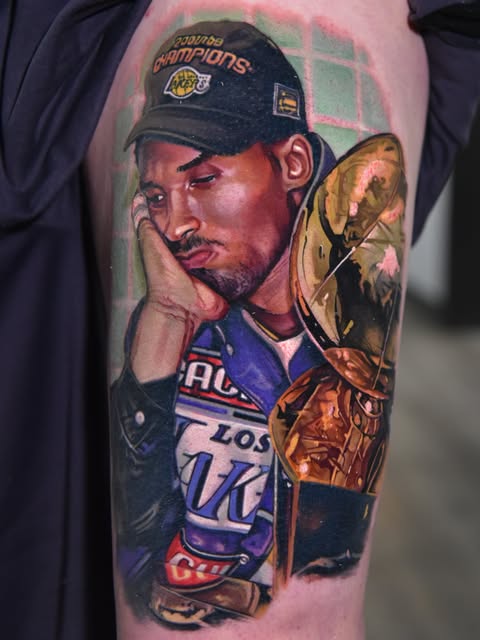 A basketball player wearing a Lakers jersey and championship cap holding the Larry O'Brien trophy on the upper arm.