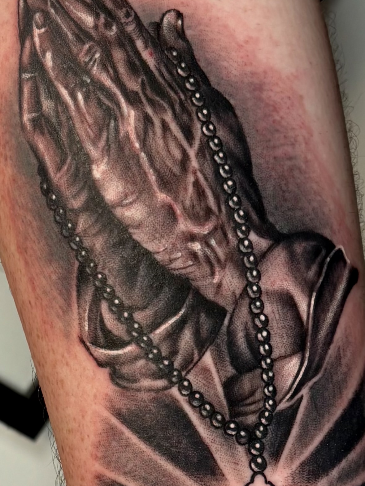Black and grey portrait tattoo of a woman with wavy hair wearing draped fabric and pearl beaded chains on the upper arm.