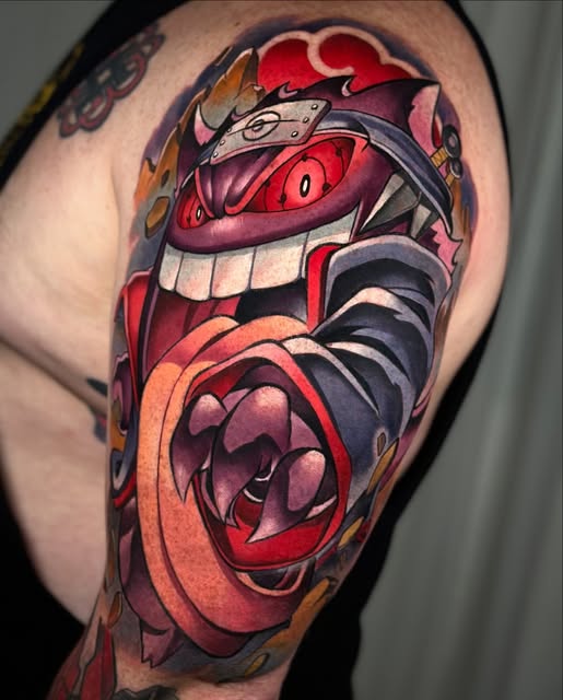 Colorful shoulder tattoo of a grinning red mechanical creature with sharp teeth and orange rose elements, featuring bold reds, purples, and blacks.