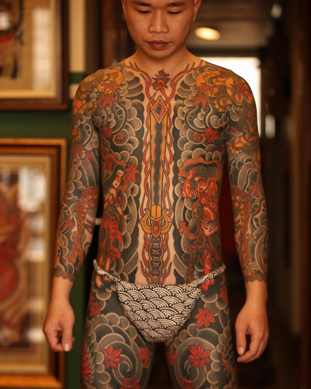 Full-body Japanese-style tattoo featuring dragons, mythological figures, maple leaves, ornamental waves, and central vertical design on chest and torso.