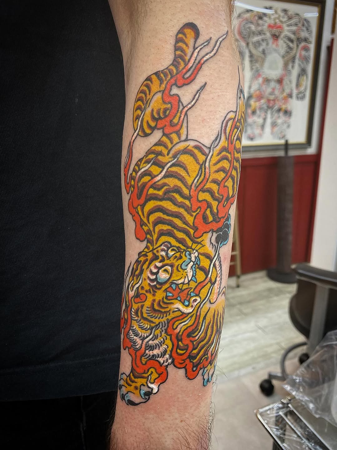 Yellow and orange tiger with flowing red and blue flames, Japanese traditional motif on forearm sleeve.