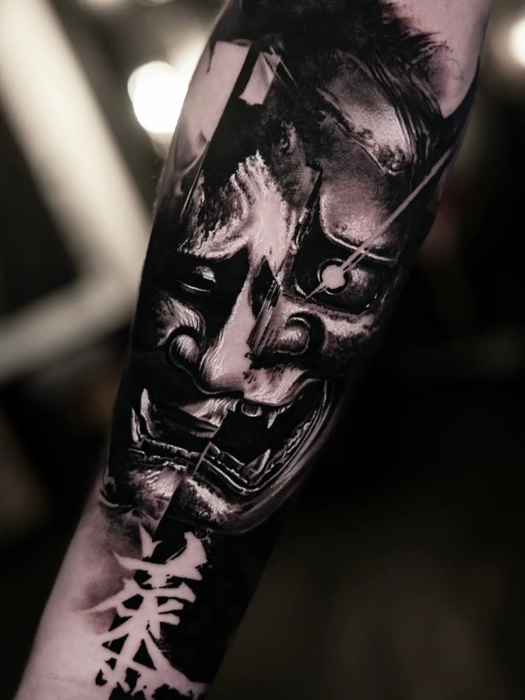 Monochrome portrait tattoo of a bearded man's face with detailed shading on the forearm, accompanied by a small geometric symbol below.