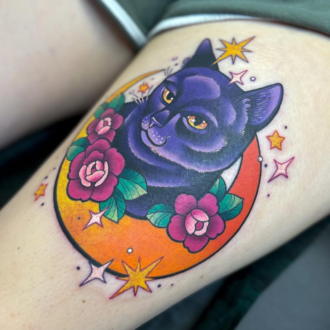 A purple cat with golden eyes nestled in a crescent moon surrounded by pink roses and stars on the leg.