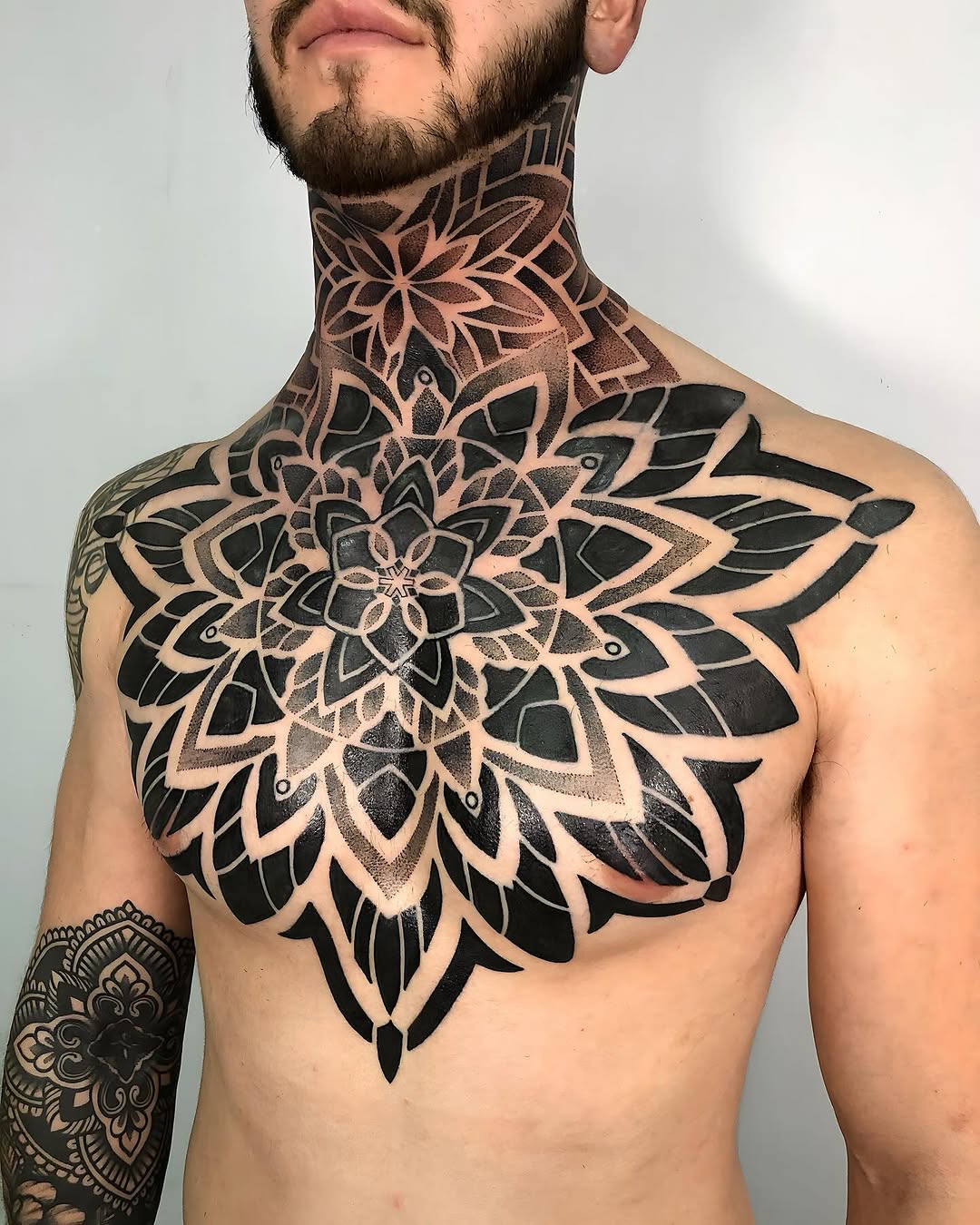 Large symmetrical mandala-style chest and neck tattoo with black and grey geometric linework featuring layered petal patterns.