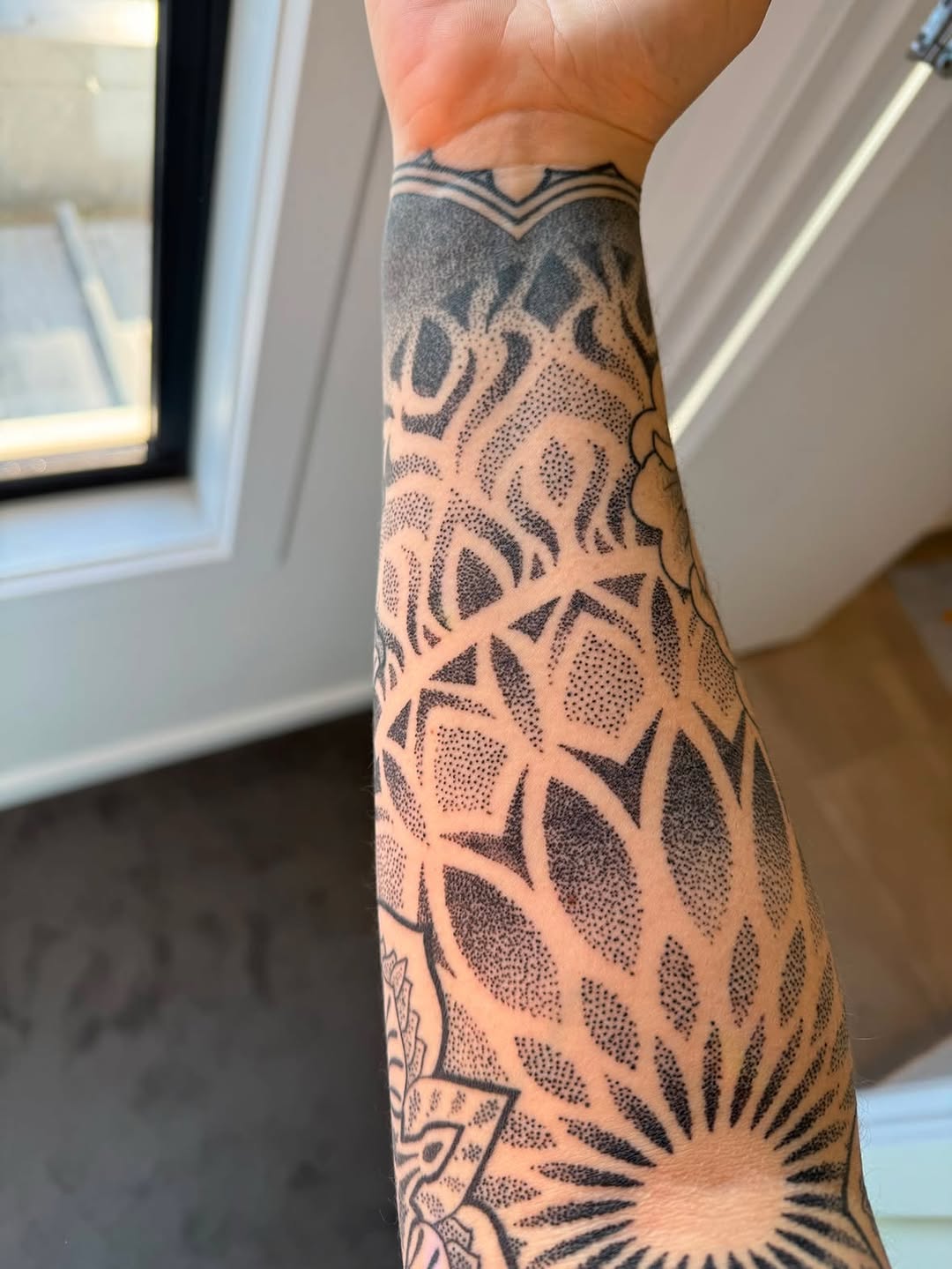 Geometric dotwork and linework tattoo covering forearm with mandala-like pattern and radiating sun motif at wrist.