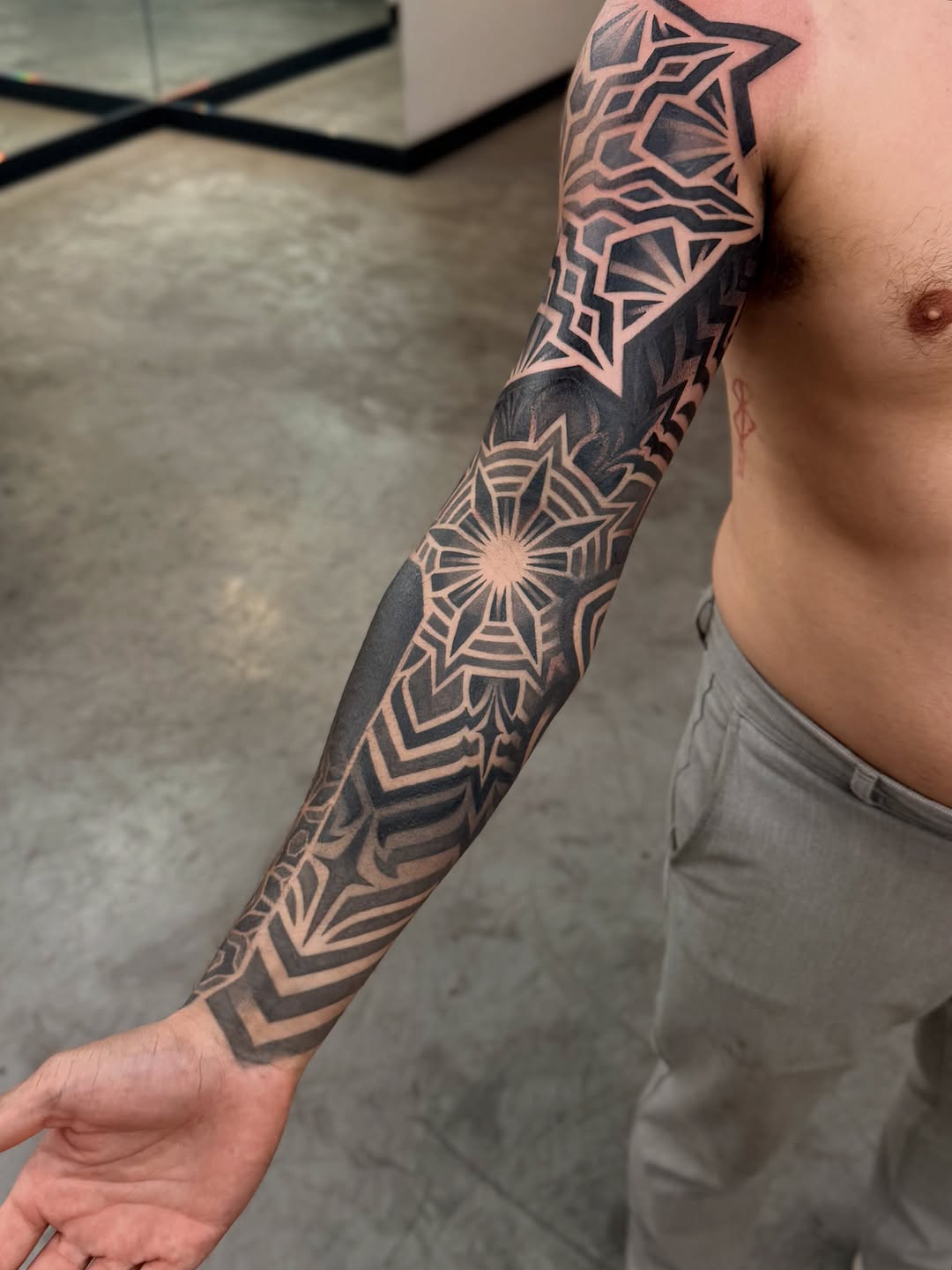 Full-sleeve geometric mandala and star pattern tattoo with symmetrical linework and dotwork stippling on forearm and upper arm.