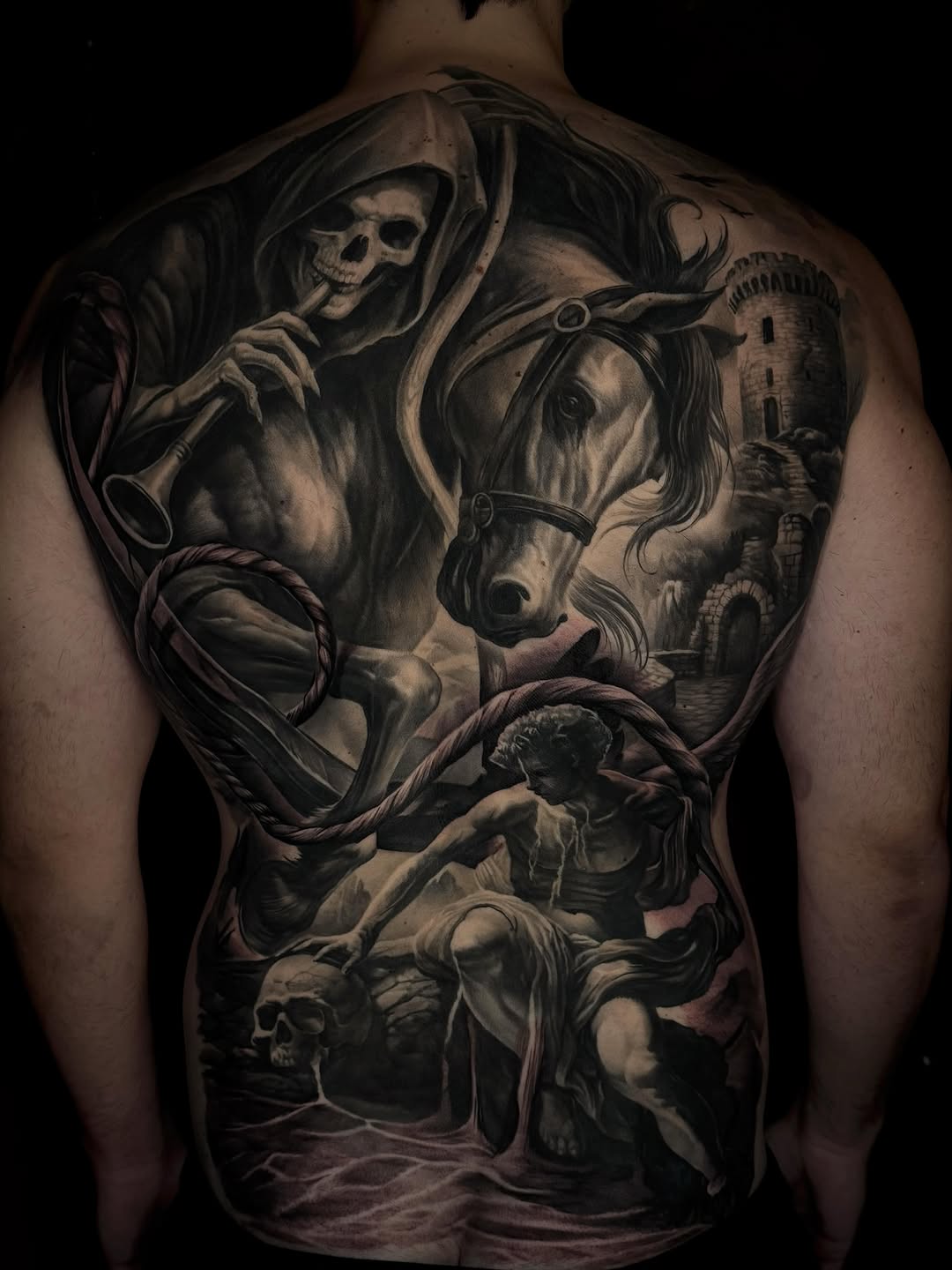 Full back tattoo of a hooded skeletal grim reaper on horseback holding a rope, with a castle tower, drowning figures, and a skull.