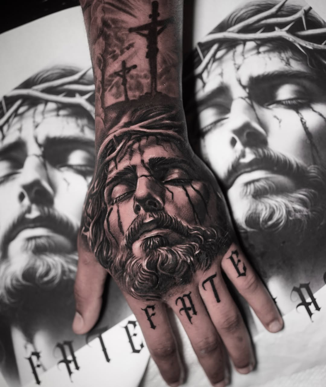 Black and grey hand tattoo depicting Jesus Christ wearing a crown of thorns, with crucifixion scene on wrist and 'FATE' lettering on fingers.