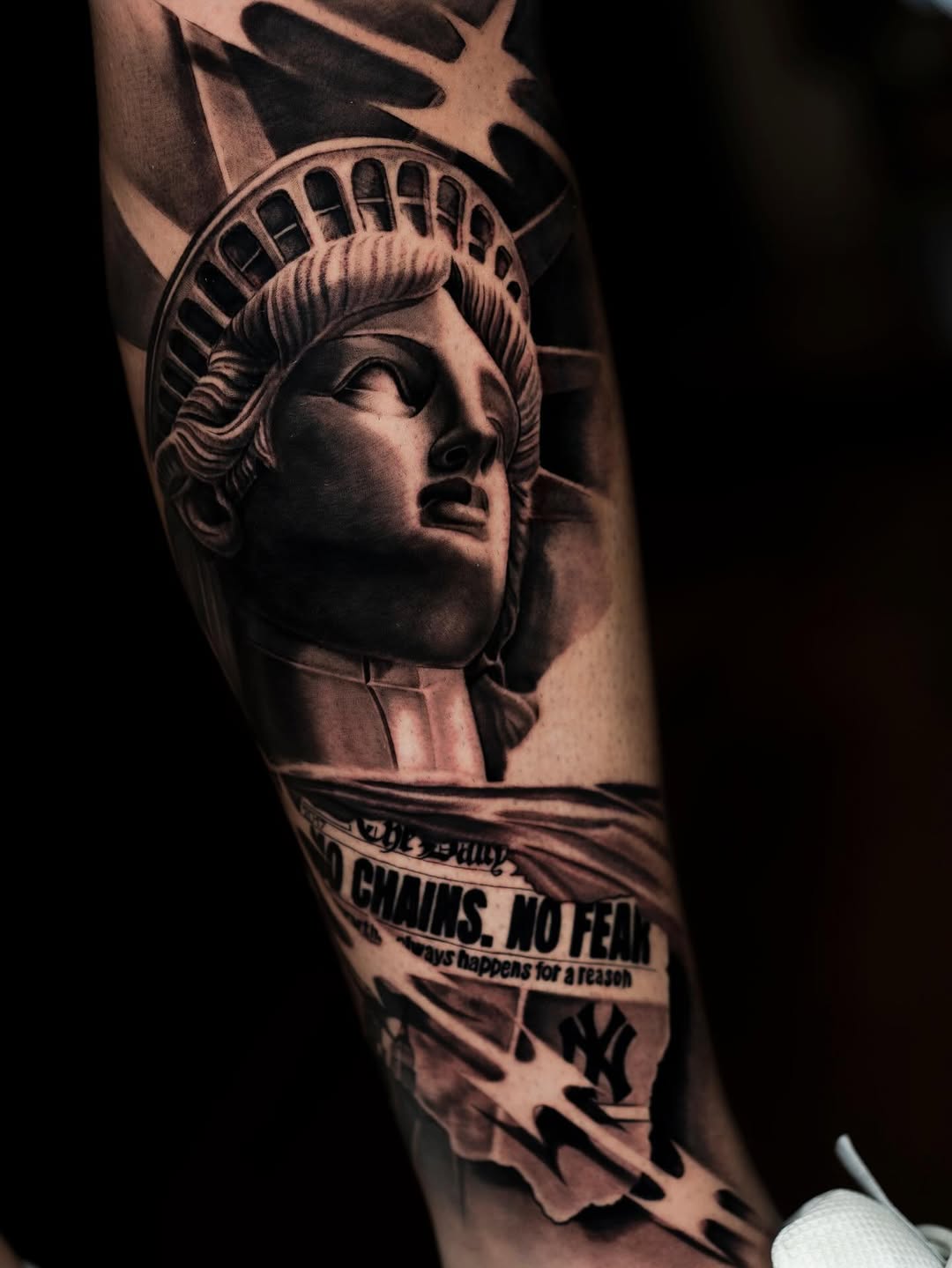 Statue of Liberty head portrait with crown and torch, banner text below, on leg in black and grey realism.