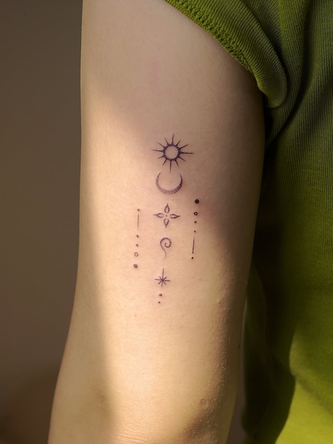 Delicate celestial tattoo featuring sun, crescent moon, four-pointed star, spiral, and decorative dots arranged vertically on the thigh.