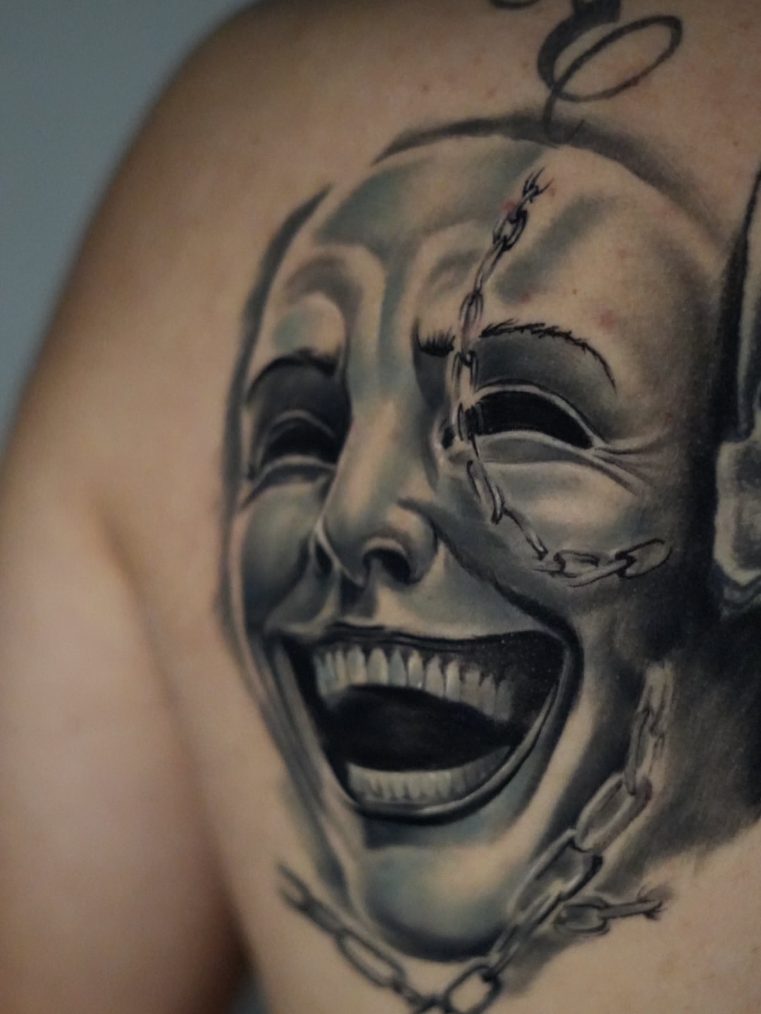 Black and grey realist tattoo of two expressive faces with open mouths and stitched details on upper arm.