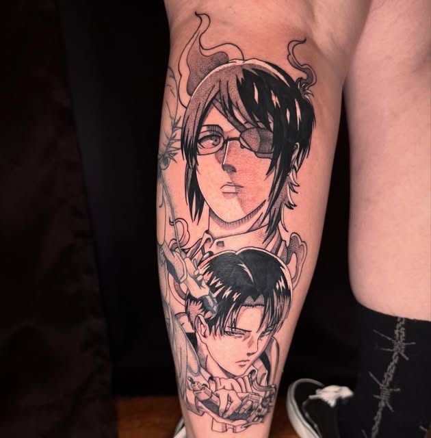 Two anime characters with dark hair and glasses tattooed on a calf, surrounded by decorative floral and vine elements in black ink.