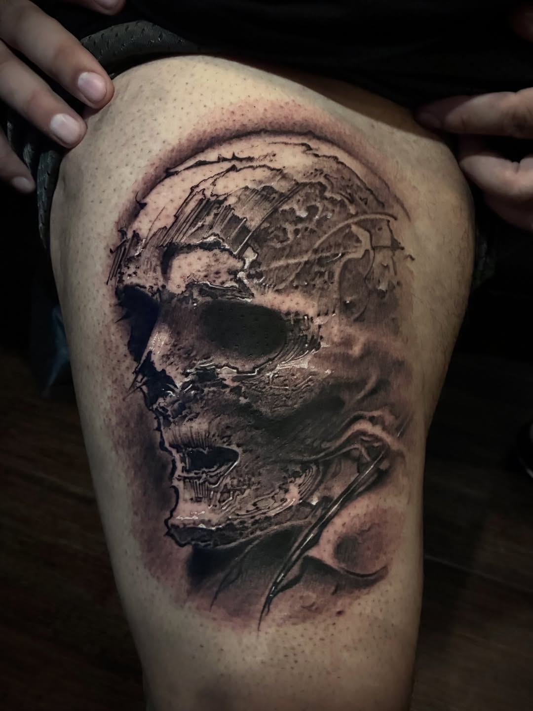 Black and grey skull tattoo with detailed shading and anatomical features on upper thigh.