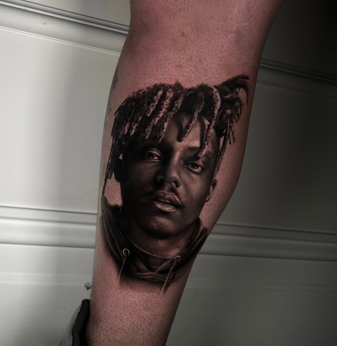 Black and grey portrait tattoo of a man's face with textured hair on forearm, realistic shading and detail.