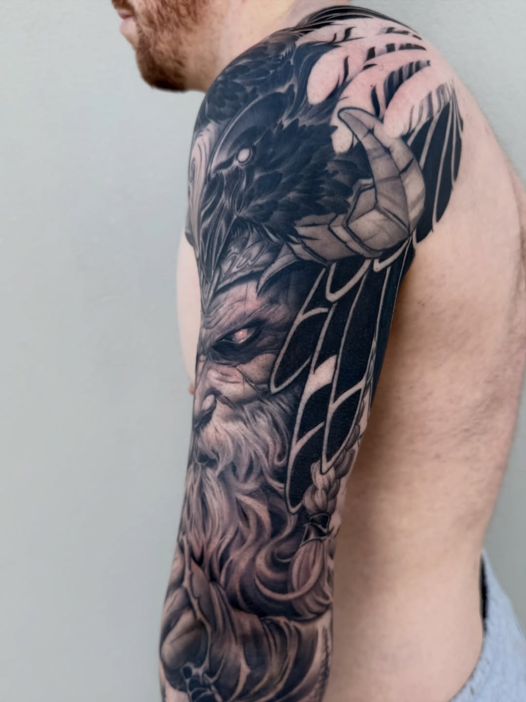 Full sleeve tattoo featuring a bearded mythological face with an eagle and intricate feather details in black and grey shading.