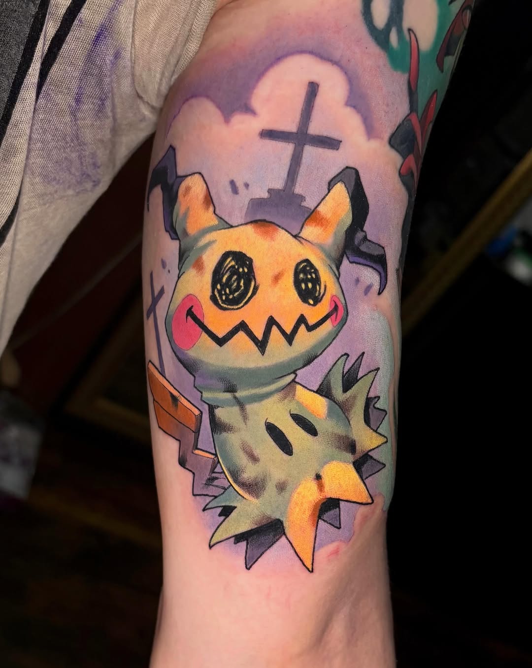 Stylized Pikachu character with exaggerated features and a cross on purple background, upper arm placement.