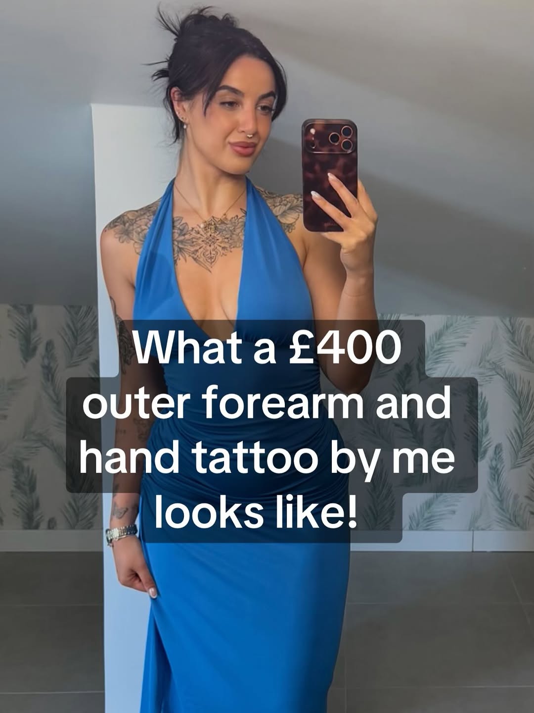 Black and grey ornamental chest and outer forearm tattoo with intricate geometric and floral patterns on a person wearing a blue dress.