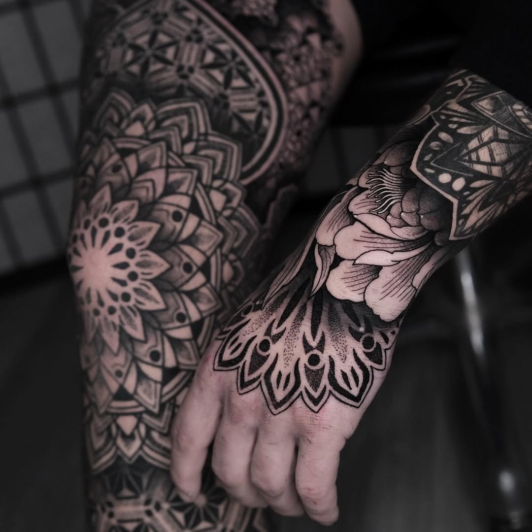 Intricate black mandala and ornamental geometric patterns covering forearm and hand with symmetrical linework and dotwork stippling details.