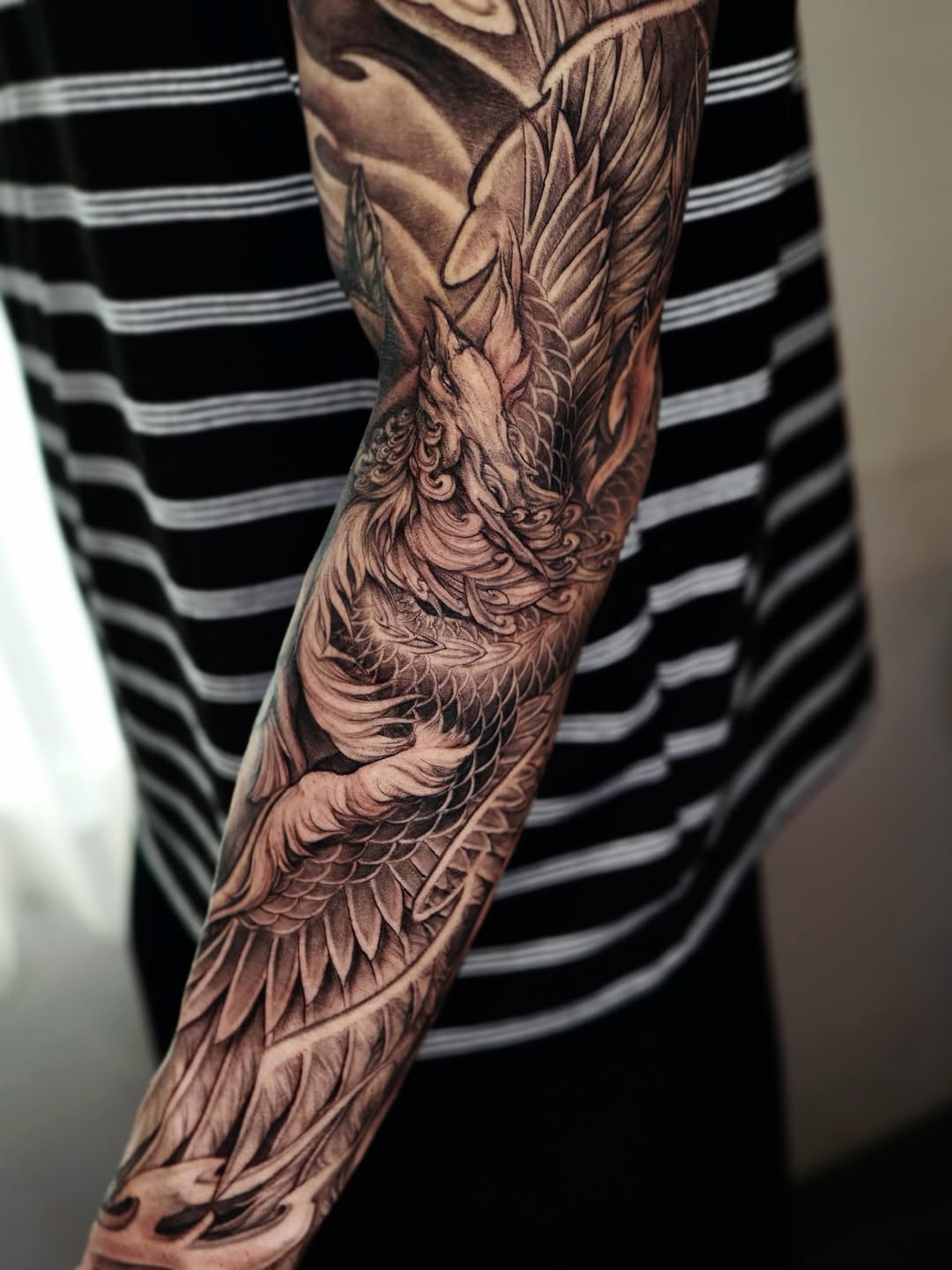 Black and grey phoenix tattoo with detailed feathers and scales covering the entire forearm in realistic shading.